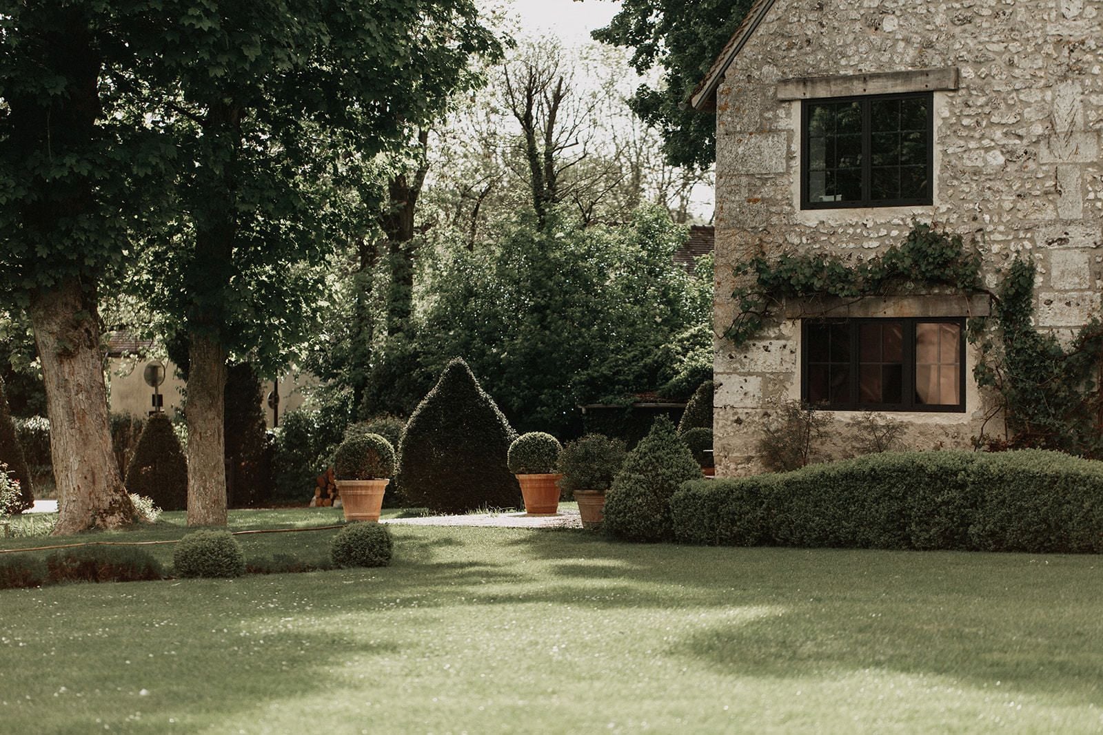 A stone building with a window and a door, surrounded by well-maintained hedges and trees.
