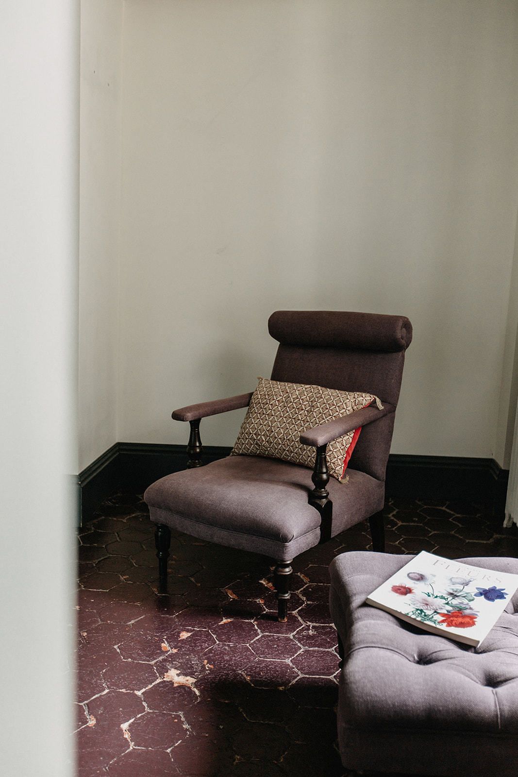 Une chaise avec un coussin à motifs et un magazine posé sur un pouf rembourré.