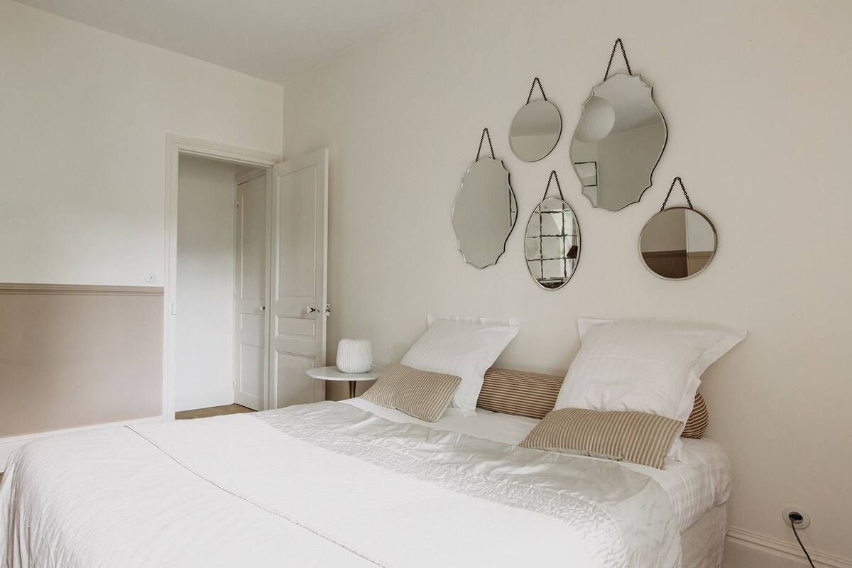 Une chambre à coucher avec un grand lit, une literie blanche et un miroir mural au design original.