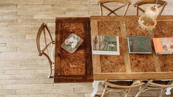 Une table à manger en bois, dotée d’un aspect rustique, est accompagnée de quatre chaises en bois. Sur la table, on trouve trois livres et un plateau sur lequel est posé un objet décoratif.
