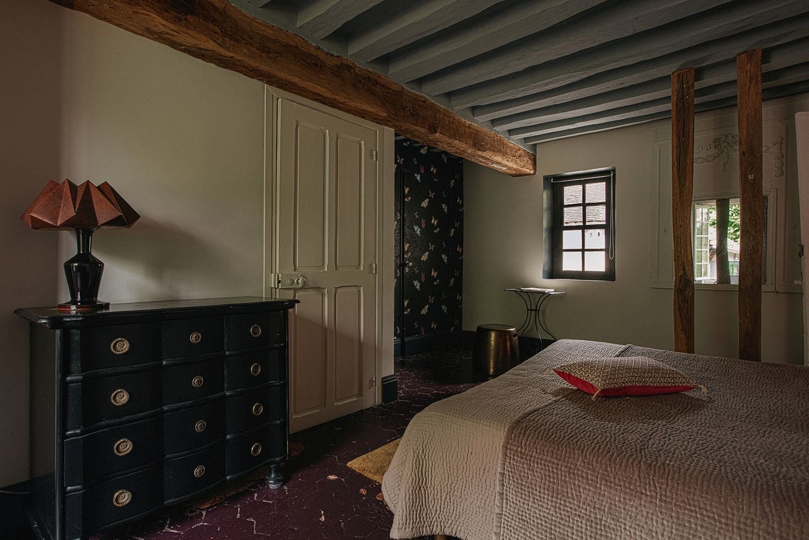 Une chambre à coucher avec un lit, une commode, une lampe, une fenêtre et une porte.