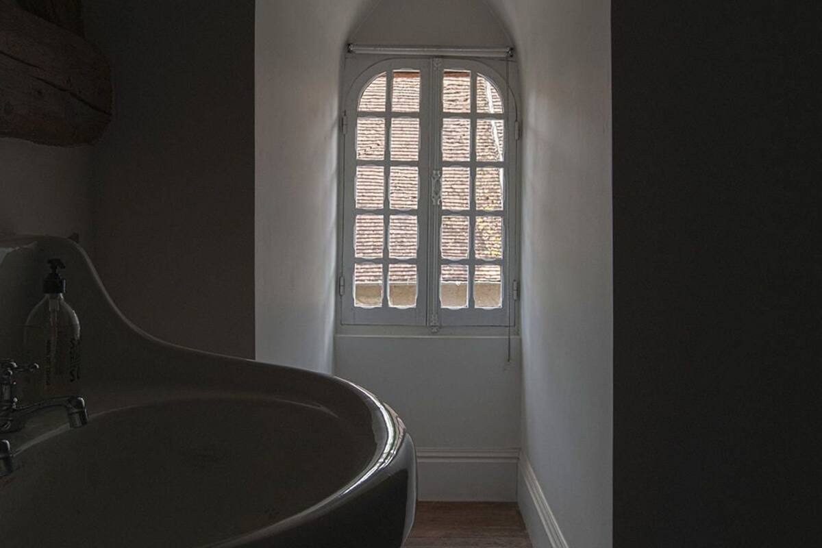 Un couloir étroit, avec une grande fenêtre en arc de cercle au fond, un plancher en bois et un grand évier avec un robinet.