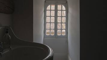 A narrow hallway with a large arched window at the end, a wooden floor, and a large sink with a faucet.