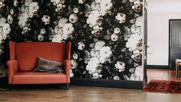 Una habitación con papel tapiz floral oscuro, un sillón rojo con cojín y suelo de madera.