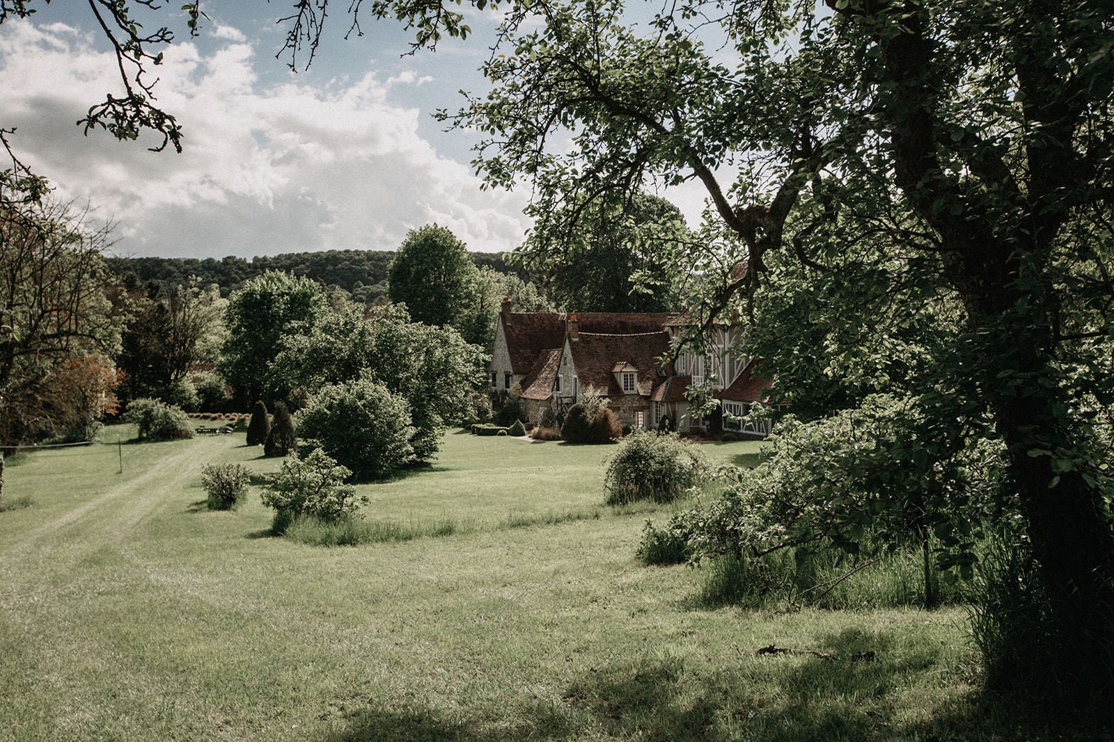 Een landelijk landschap met een traditioneel huis, omringd door bomen en een grasveld.
