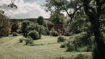 Een landelijk landschap met een traditioneel huis, omringd door bomen en een grasveld.