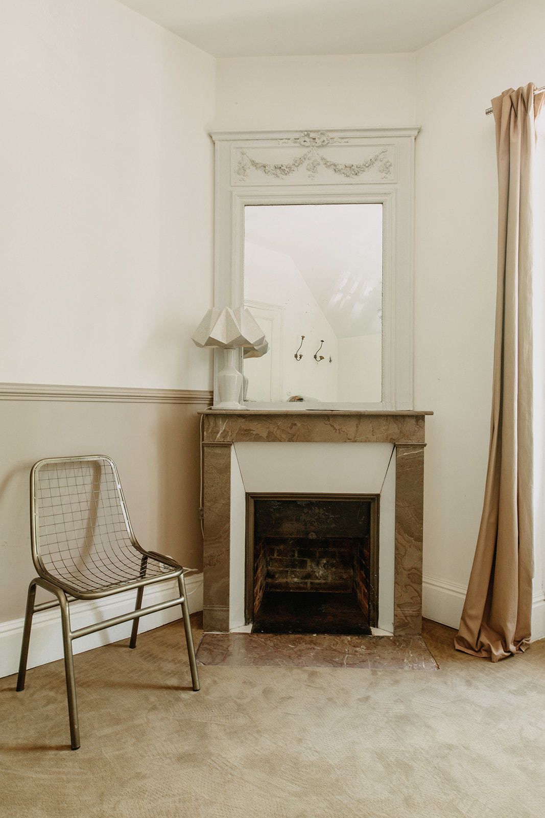 Una habitación con chimenea blanca, una silla y una ventana con cortina.