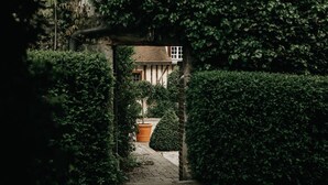 A pathway leading to a house surrounded by dense greenery and a stone wall. - La Dime de Giverny - Chambres D'hôtes (Giverny)