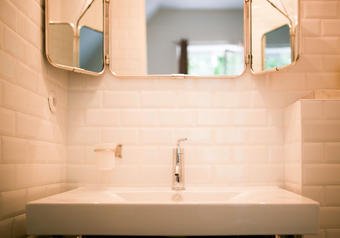 A bathroom with a white sink, two mirrors, and a white tiled wall.