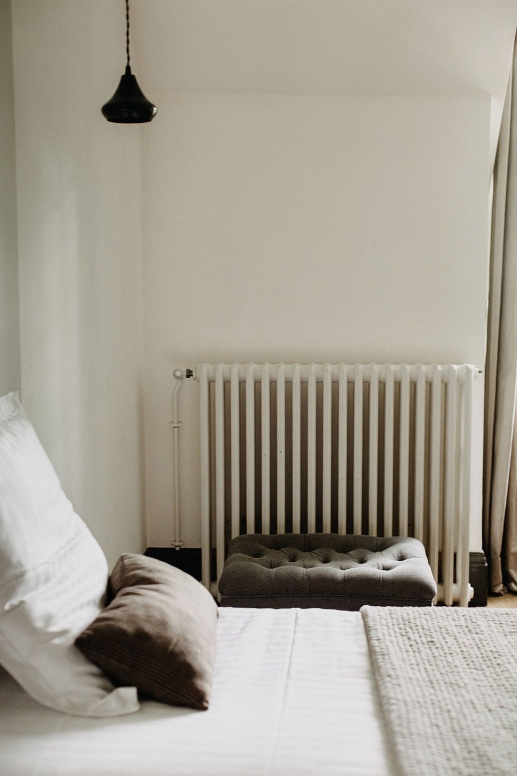 A bedroom with a bed, a radiator, a bedside lamp, and a window with curtains.