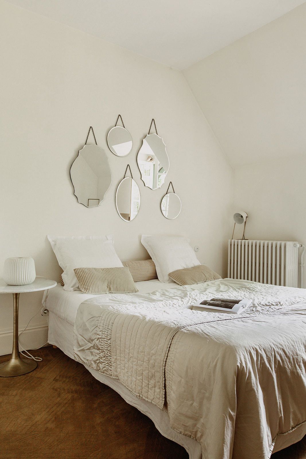 A bedroom with a bed, bedside table, and wall-mounted mirrors.