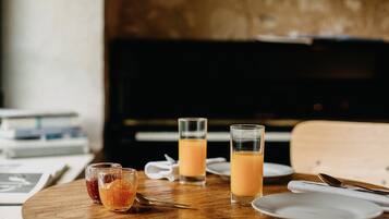 Ett träbord med tre glas apelsinjuice och ett glas med en mörk vätska, troligen te eller kaffe, på en vit tallrik.