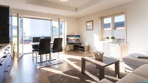 A modern living room with a dining area, a flat-screen TV, and a balcony with a view.