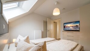 A bedroom with two beds, a TV on the wall, a skylight, and a radiator.