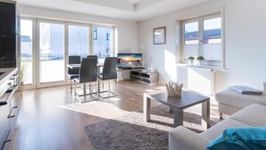 A modern living room with a flat-screen TV, a dining area with chairs, a sofa, and a coffee table.
