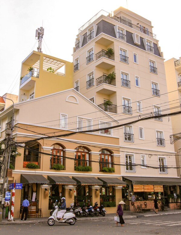 Un immeuble à plusieurs étages doté de balcons, avec un restaurant au rez-de-chaussée et des scooters garés à proximité.