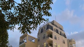 A multi-story building with balconies, a ground-level restaurant with outdoor seating, and a street with parked motorcycles and cars. - The Lighthouse (Can Tho)