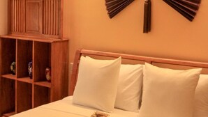 A neatly made bed with white linens and pillows, a wooden headboard, and a wall-mounted fan. - The Lighthouse (Can Tho)