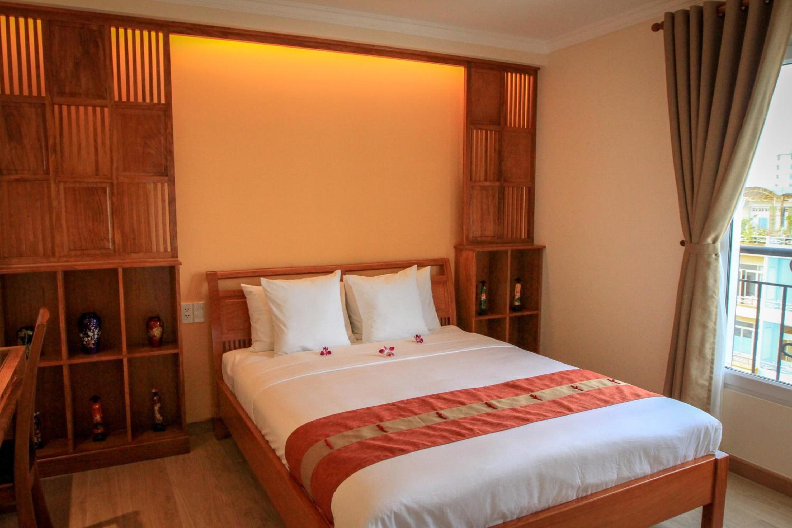 A neatly arranged bedroom with a wooden bed, a shelf with decorative items, and a window with curtains.