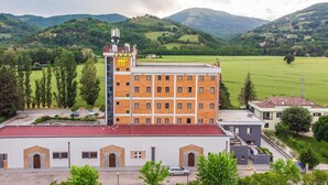 A multi-story hotel with a red roof, surrounded by green fields and hills. - Hotel PentHouse (Perugia)