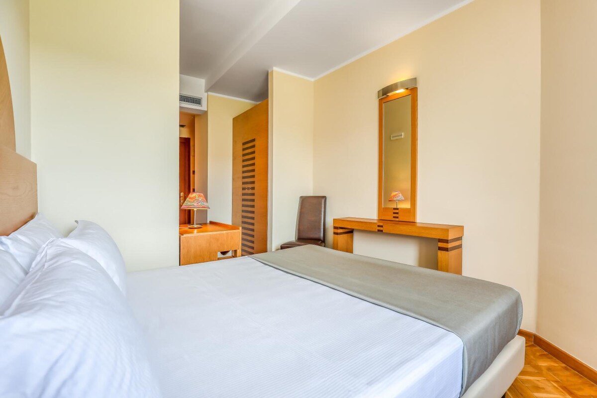 A hotel room with a bed, a desk, a chair, and a mirror.