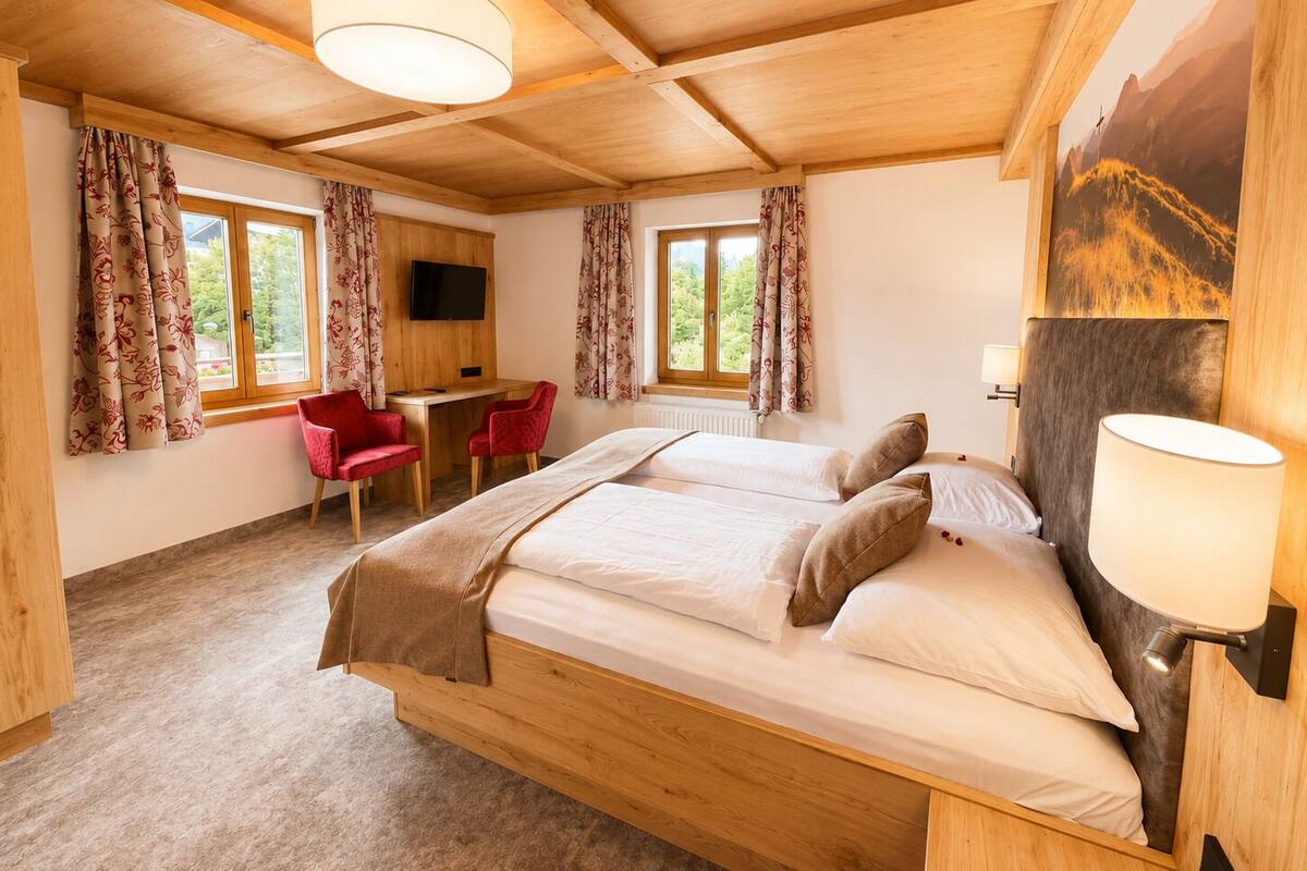 A bedroom with a wooden bed, two red chairs, a desk, a TV, and a painting on the wall.