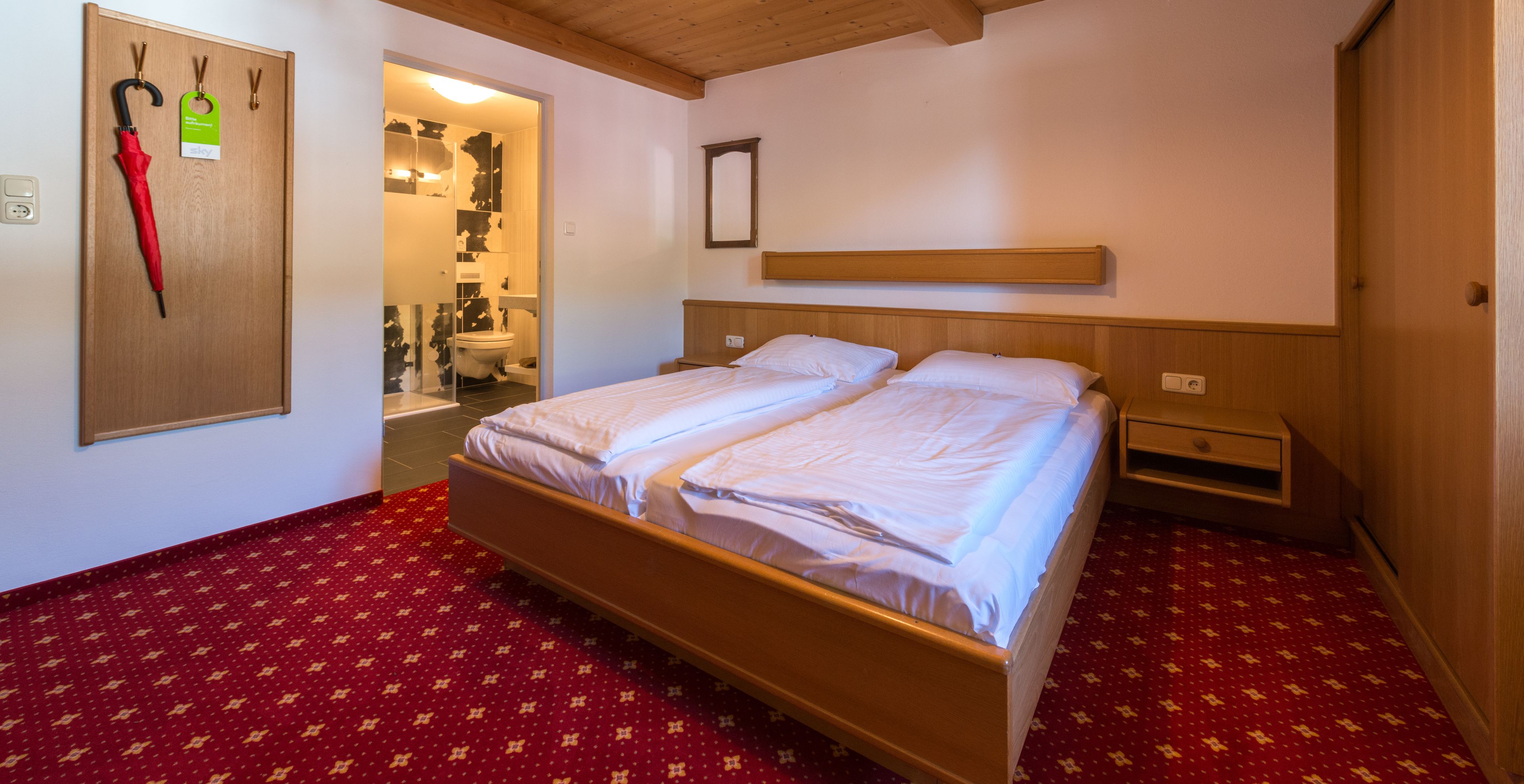 A double bed with a wooden headboard, a bedside table, and a red patterned carpet.