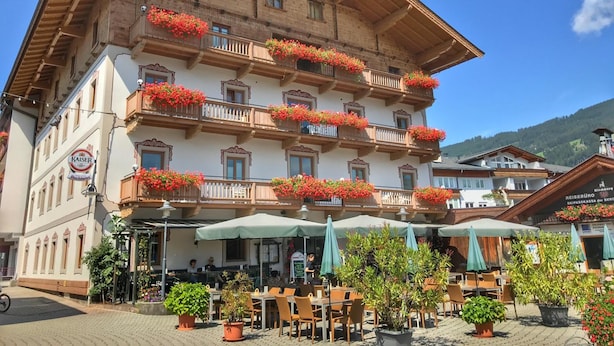 Un edificio de varios pisos con balcones decorados con flores rojas, asientos exteriores con sombrillas y un letrero que indica una marca de cerveza local.