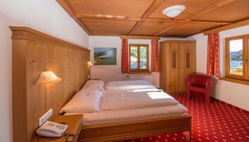 Un dormitorio con una cama de madera, una silla roja, un armario de madera y una ventana con vistas a zonas verdes.