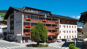 Un hotel de varios pisos con balcones, un paso de cebra y coches aparcados.