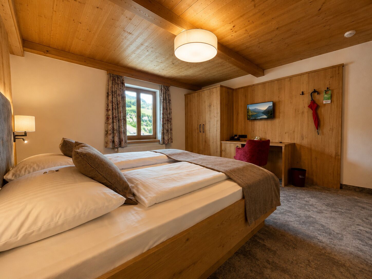 Un dormitorio con una cama de madera, una ventana con cortinas, un televisor en la pared y una silla roja.
