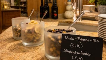 A breakfast bar with three bowls of cereal, a sign indicating 'Nuss - Beeren - Mix' and 'Studentenfutter,' and a background with bottles and a snowman decoration.