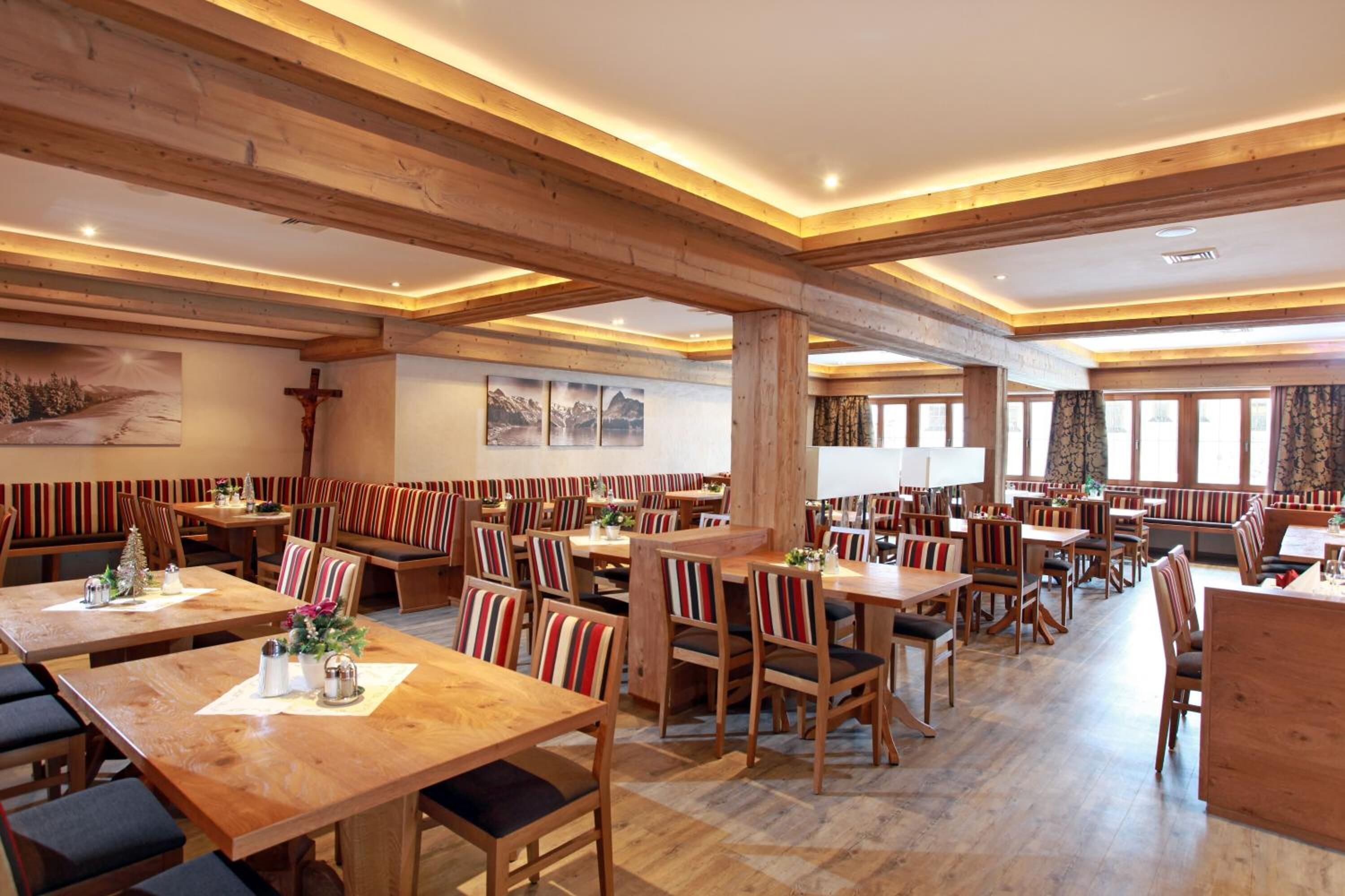 Un restaurante espacioso con mesas y bancos de madera, techos altos con vigas a la vista y grandes ventanales que dejan entrar luz natural.