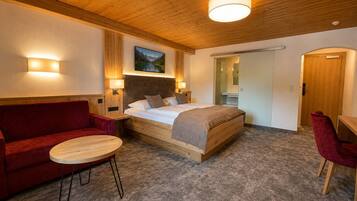 A hotel room with a wooden ceiling, a bed with a headboard, a red sofa, a small round table, and a mirror.