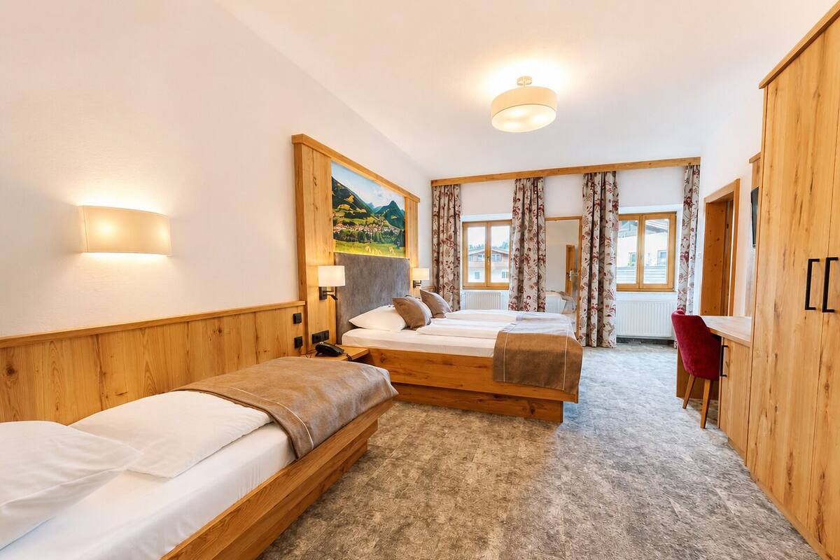 A hotel room with three beds, a wooden wardrobe, a desk, and a painting on the wall.