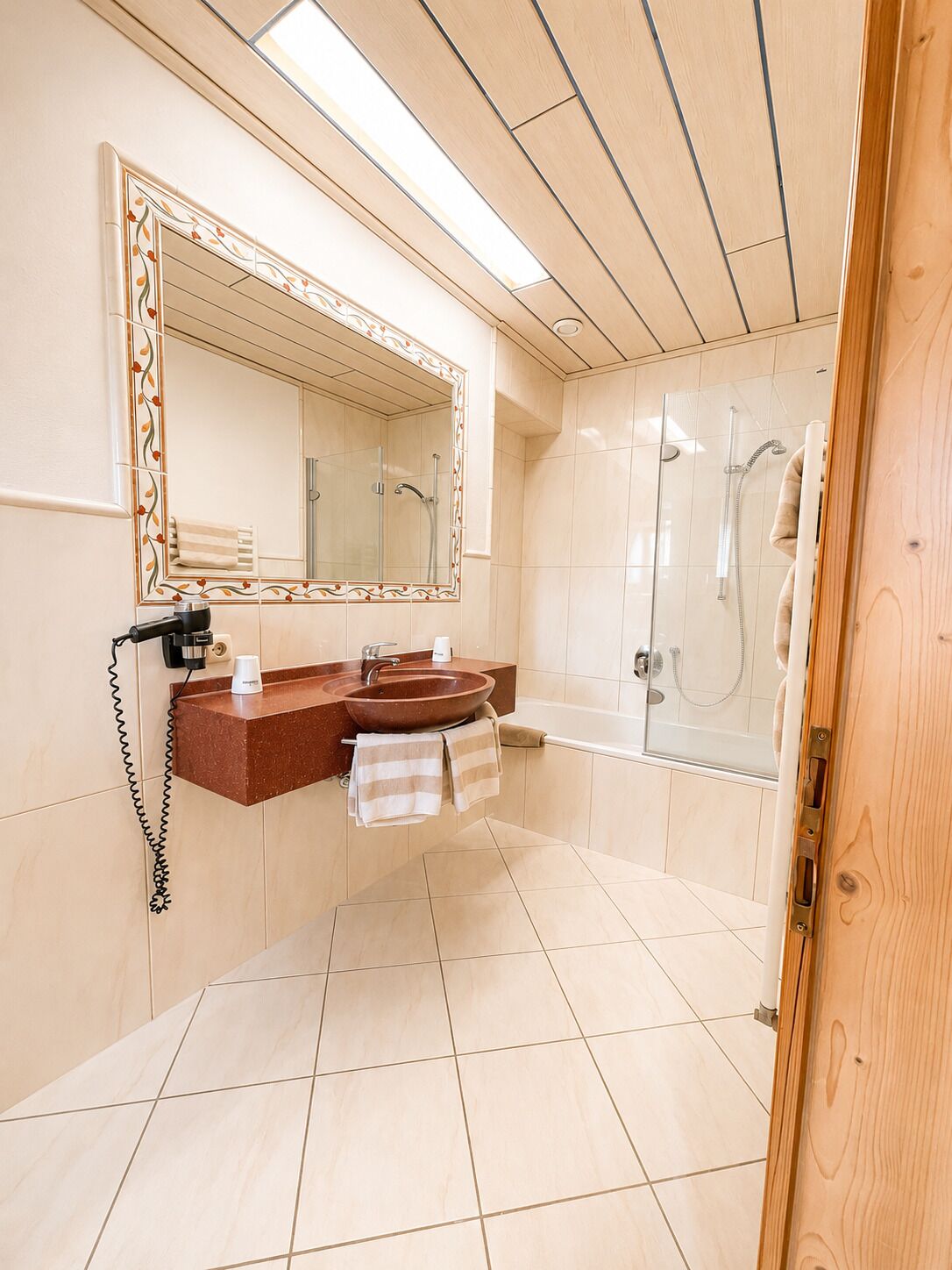Ein Badezimmer mit einem großen Spiegel, einem Waschbecken, einer Dusche und einem Handtuchhalter.