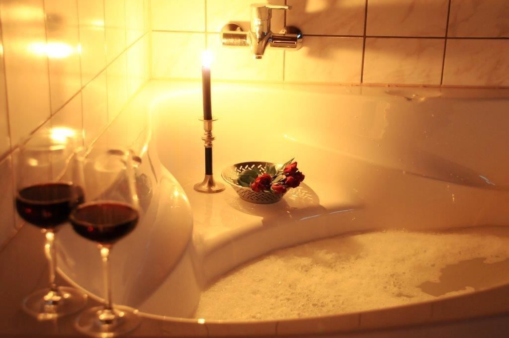 A bathtub with a candle, two wine glasses, and a bowl of flowers.