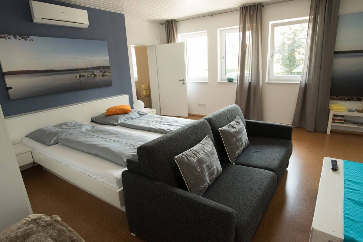 A bedroom with a bed, a grey sofa, and a TV.