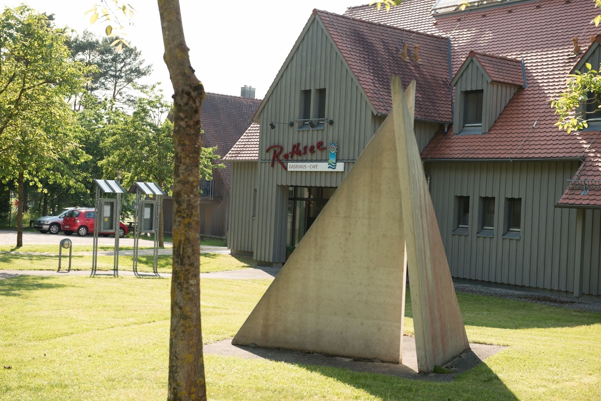 A building with a sign reading "Rothser Gasthaus - Café" and a concrete structure in front.