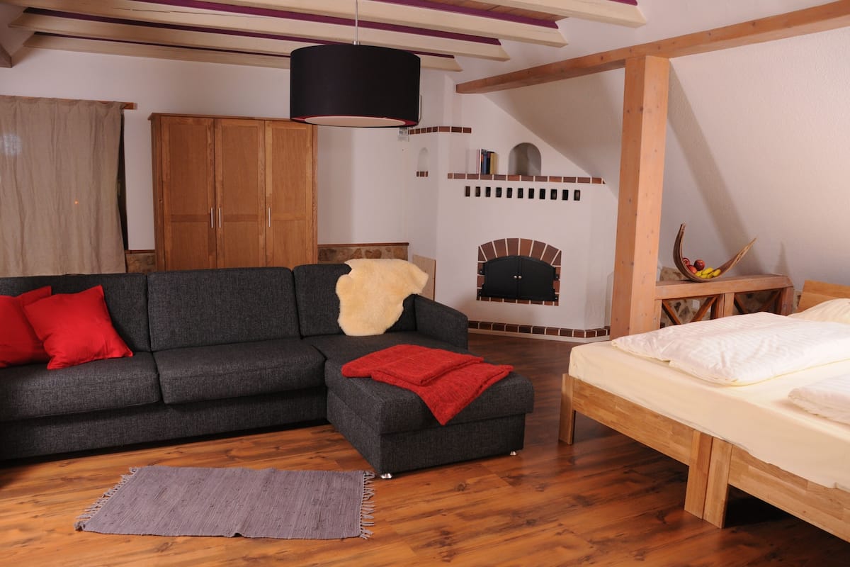 A modern living room with a sofa, a small ottoman, a bed, a fireplace, and a wooden cabinet.