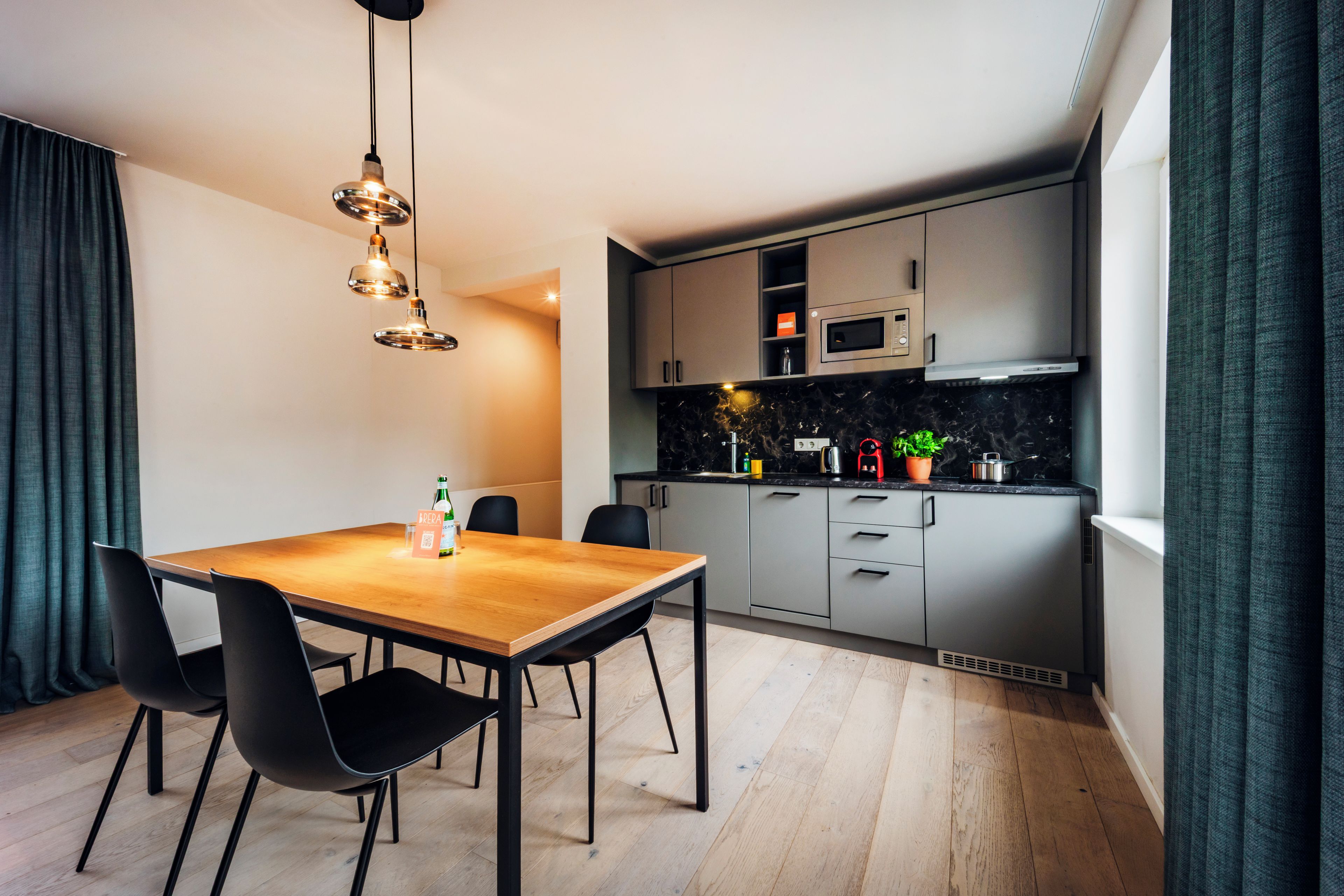 A modern kitchen with a microwave, stove, and cabinets. There is a dining table with chairs and a hanging light fixture.