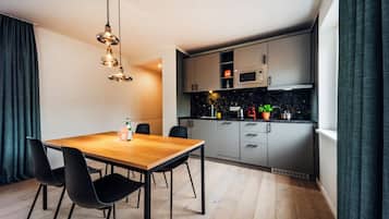Une cuisine moderne équipée d’un four à micro-ondes, d’une cuisinière et de placards. On y trouve une table à manger avec des chaises et un luminaire suspendu.