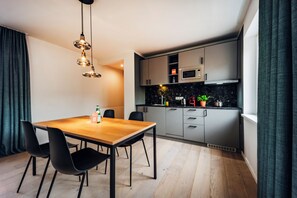Cocina moderna con microondas, estufa y alacenas. Hay una mesa de comedor con sillas y una lámpara colgante.