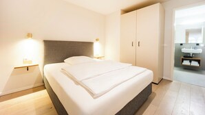 Habitación de hotel con cama, lámparas de noche, armario y baño con lavamanos.