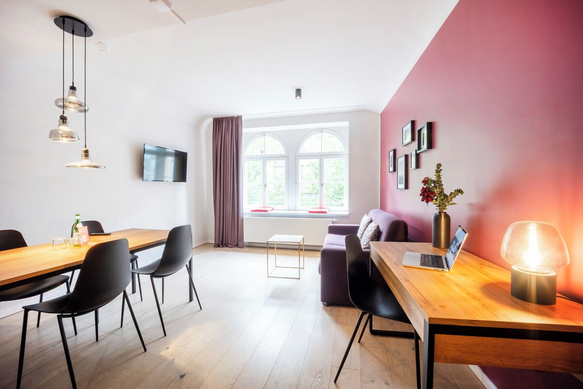 A modern meeting room with a wooden table, black chairs, a laptop, and a TV on the wall.
