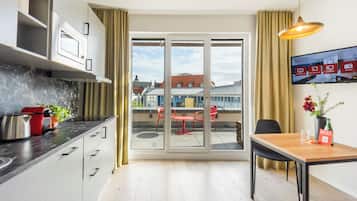 A modern kitchen with a dining area, a view of the cityscape through a glass door, and a table with a vase of flowers.