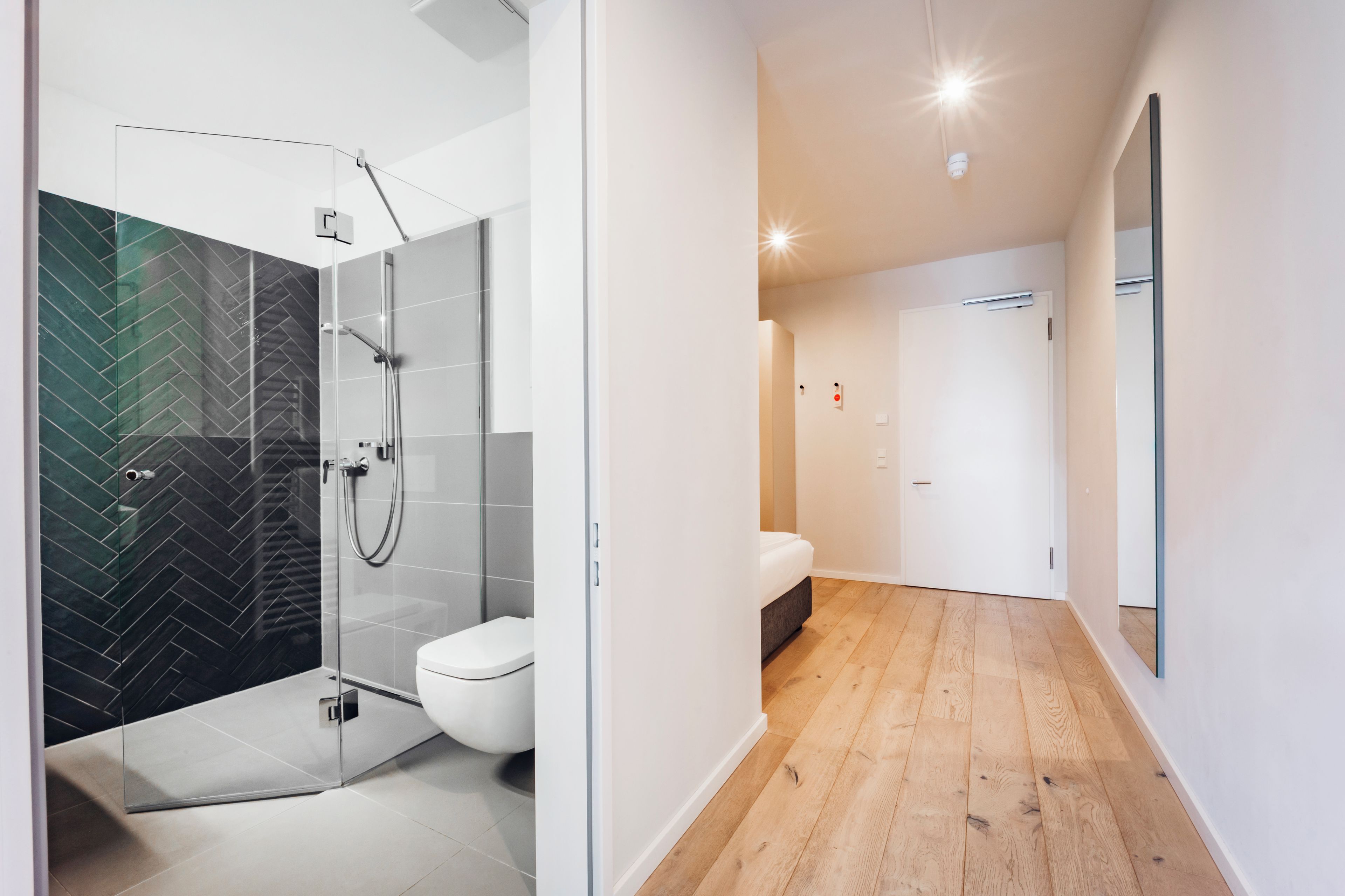 A modern bathroom with a glass shower enclosure, a toilet, and a wooden floor.