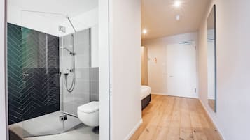 A modern bathroom with a glass shower enclosure, a toilet, and a wooden floor.