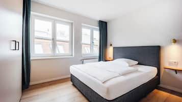 Ein modernes Schlafzimmer mit einem großen Bett, zwei Fenstern, einem Nachttisch und einer Wandleuchte.