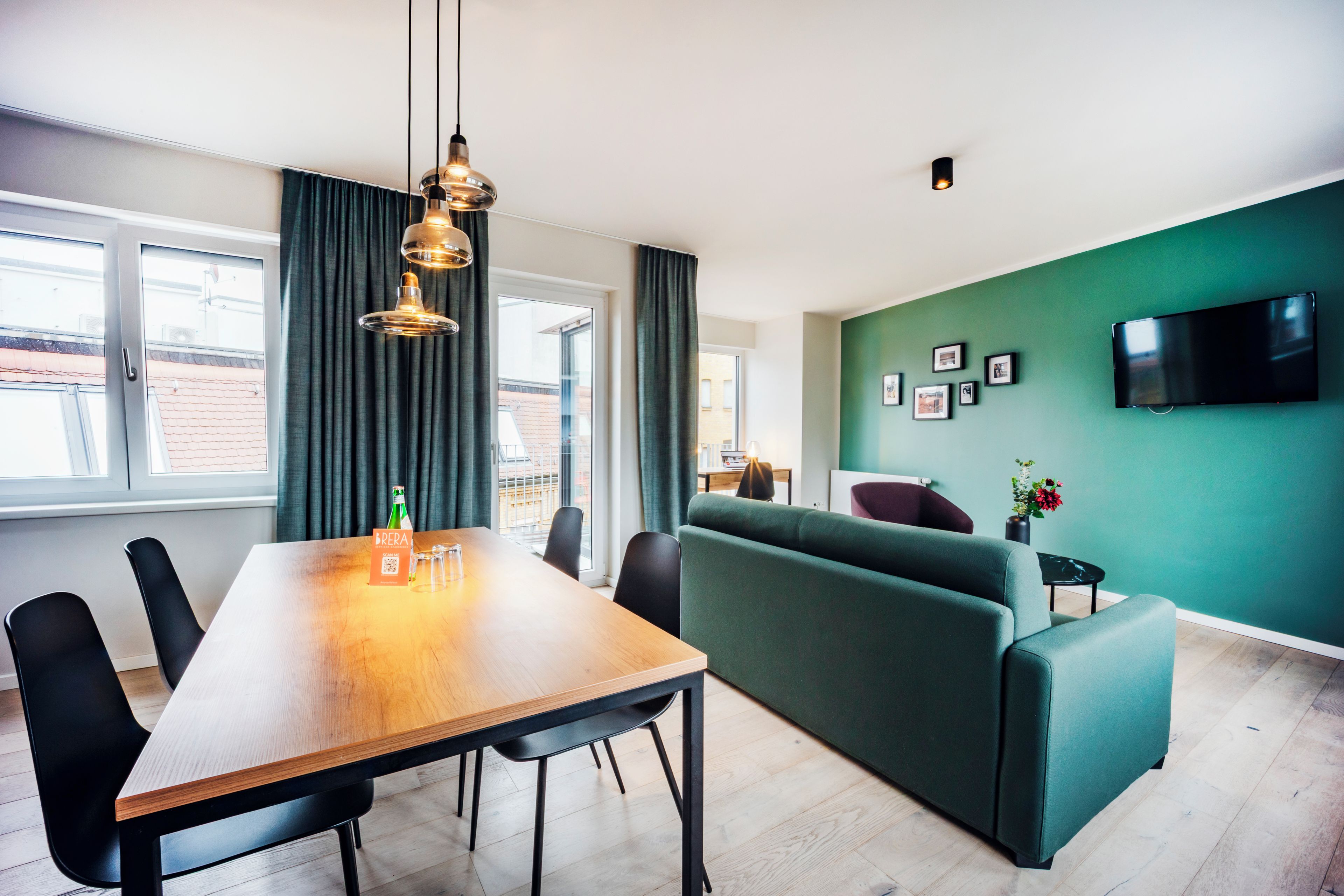 Un salon moderne avec une table à manger en bois, un canapé vert et un téléviseur à écran plat fixé au mur.